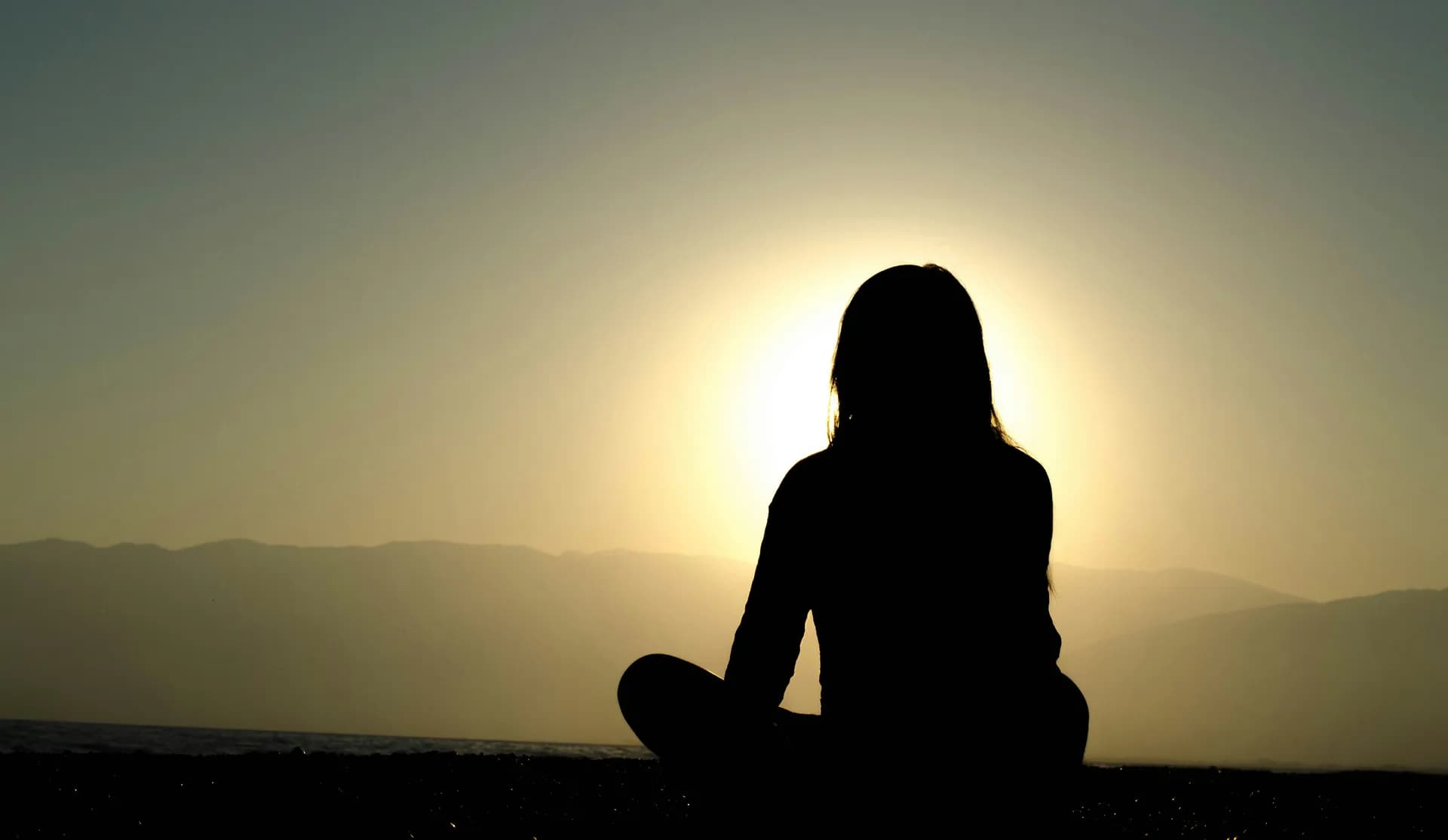 Mujer meditando en la montaña frente al sol