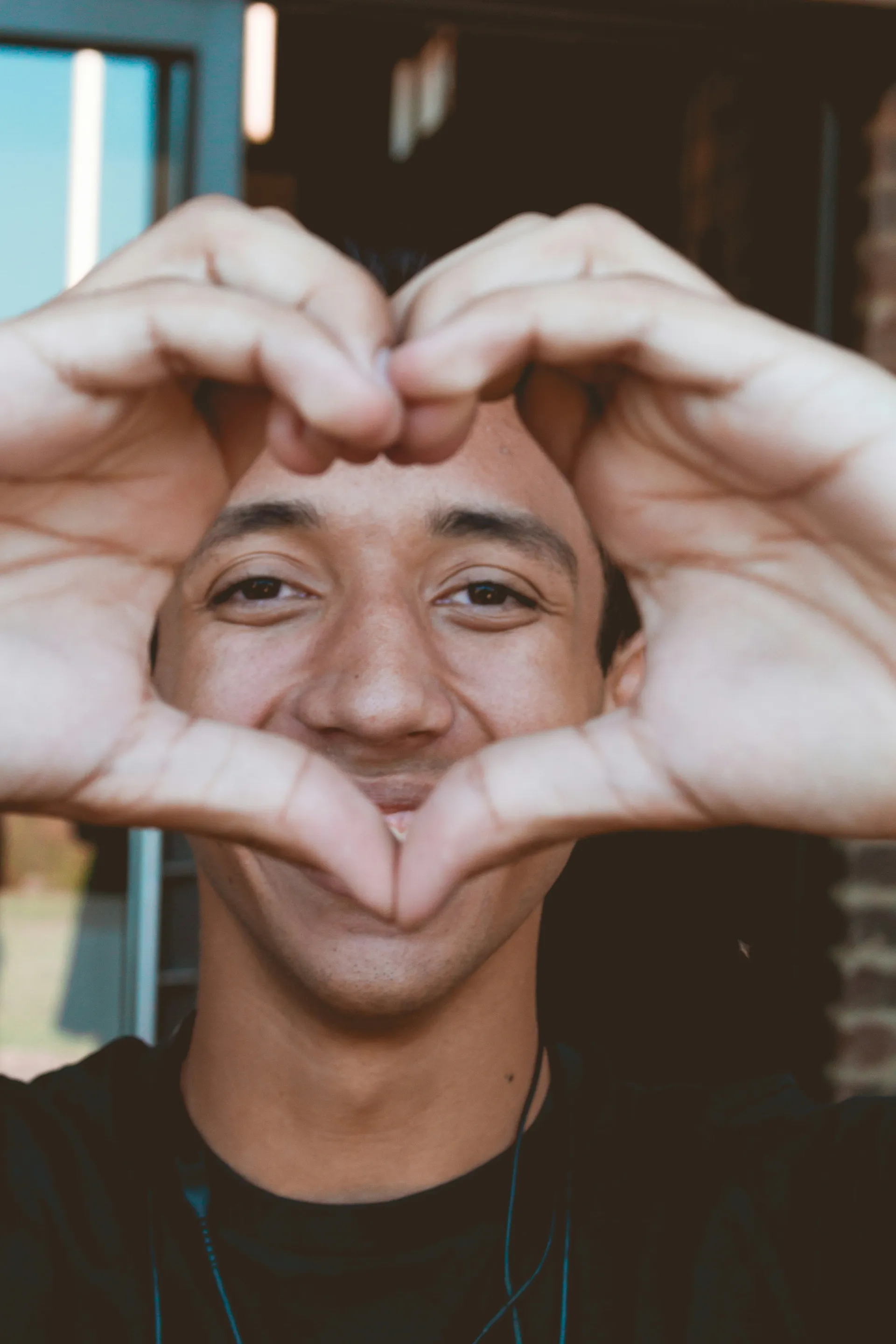 Un chico sonriendo haciendo un corazon con los dedos de las manos