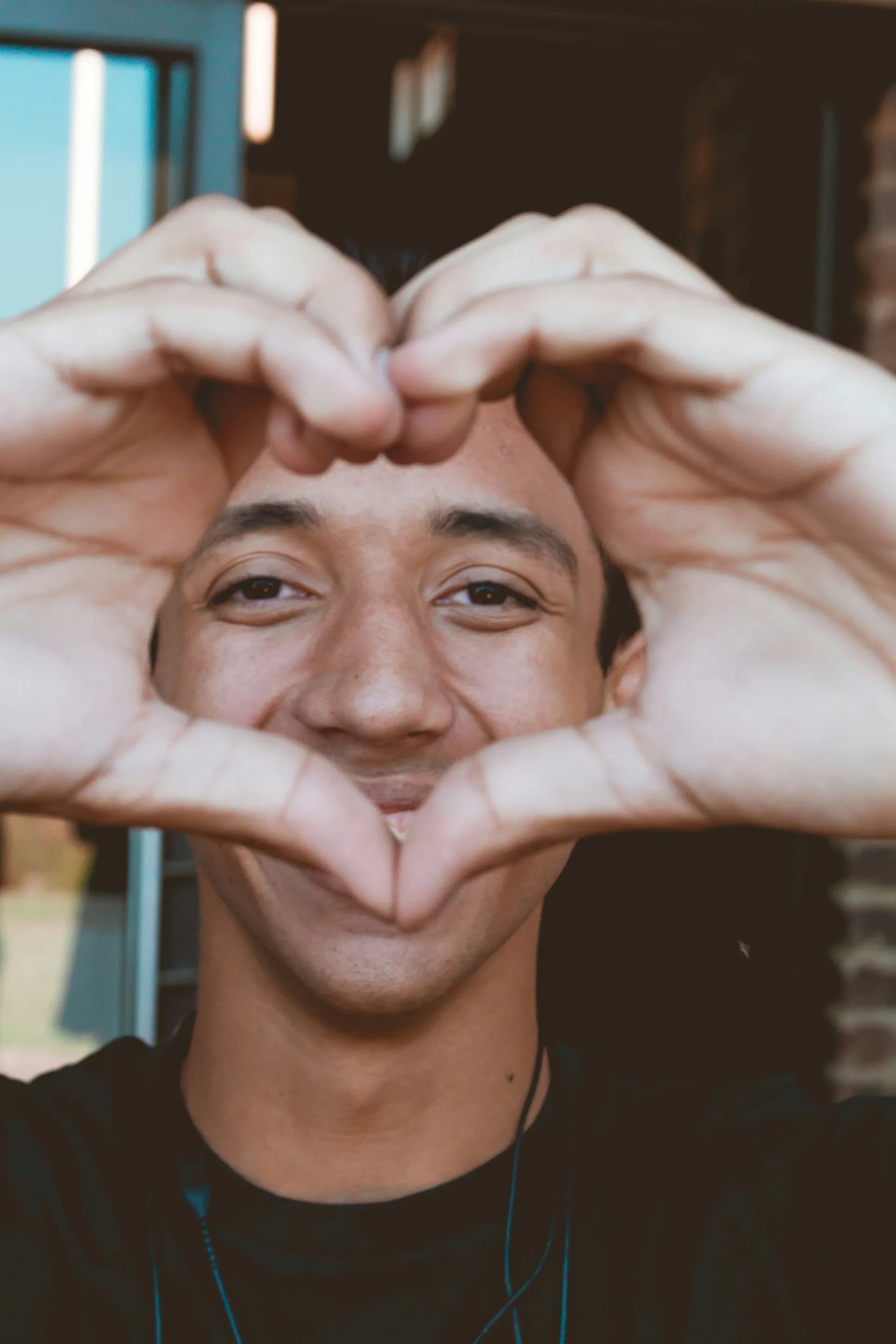 Un chico sonriendo haciendo un corazon con los dedos de las manos